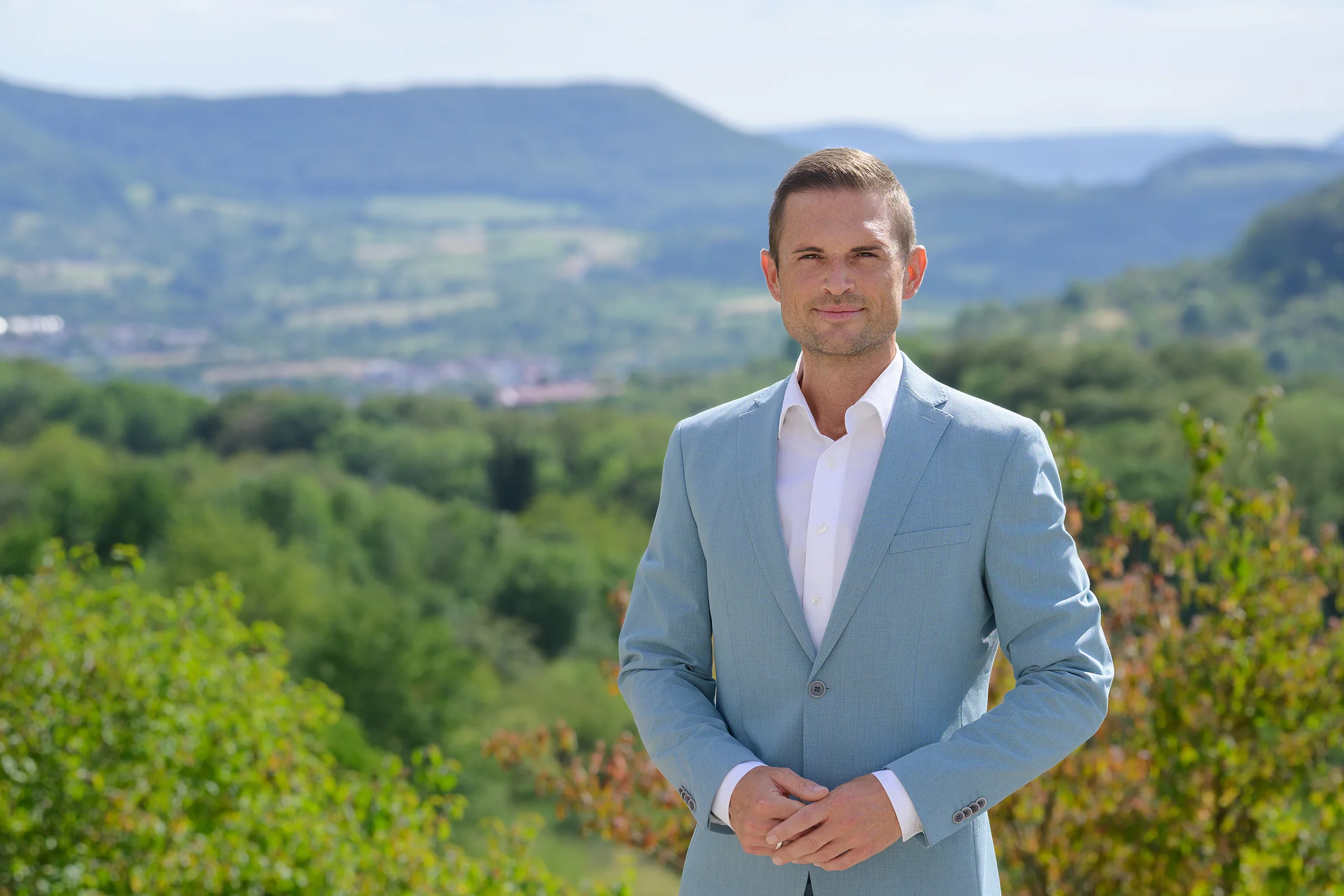 Denis Janzen im hellblauen Anzug vor der Hügellandschaft der Schwäbischen Alb